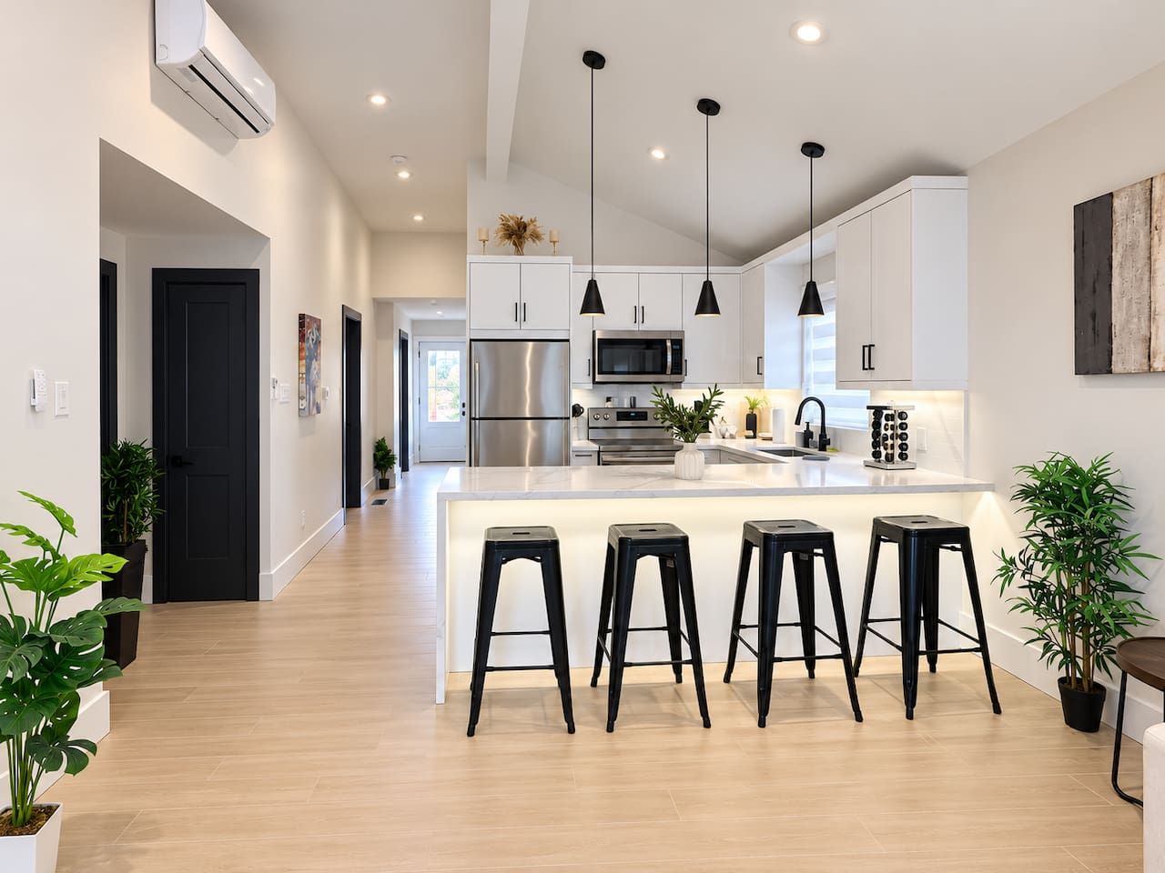 Une cuisine moderne dotée d’un îlot central, d’appareils électroménagers en acier inoxydable et de tabourets de bar noirs.
