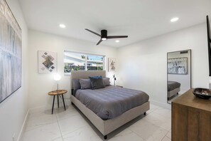 Ein Schlafzimmer mit einem Bett, einem Deckenventilator, einem Nachttisch mit Lampe und Bildern an den Wänden.