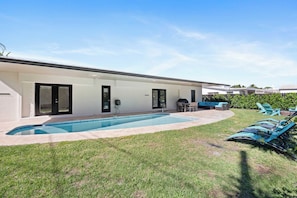 Ein modernes Haus mit Schwimmbad, Sitzgelegenheit im Freien und einem gepflegten Rasen.