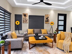 Ein modernes Wohnzimmer mit einer Couch, einem Hocker und einem Couchtisch, einem Deckenventilator und Wandbildern.