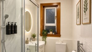 Et moderne badeværelse med en glasbrusekabine, et hvidt toilet og en håndvask med et spejl over.