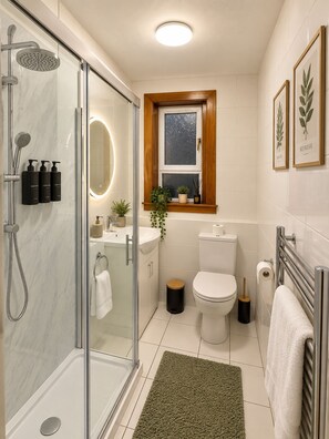 Un baño moderno con cabina de ducha de vidrio, inodoro blanco y lavamanos con espejo superior.