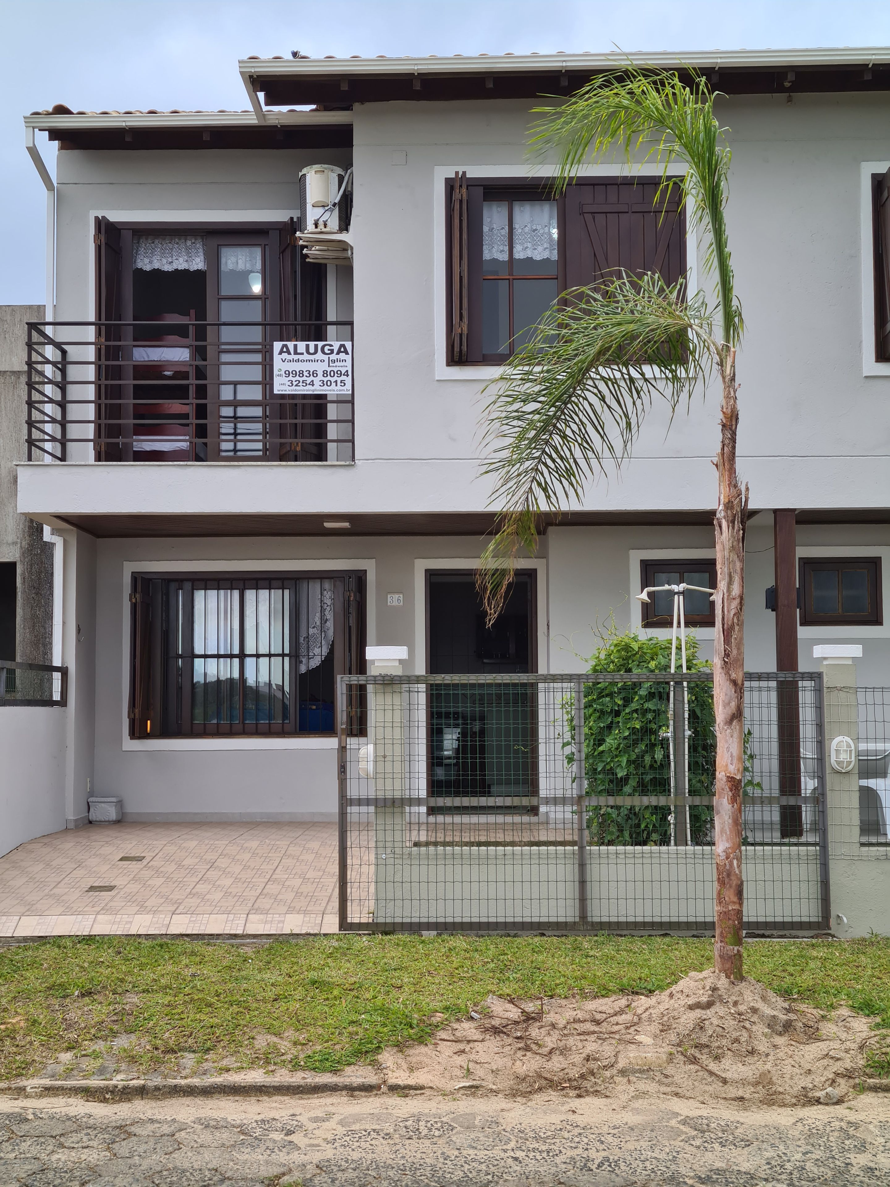 A two-story building with a balcony, a signboard, and a fenced area with a palm tree.