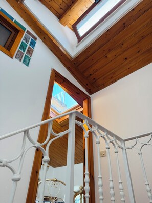 A white metal staircase with a wooden ceiling and a skylight.