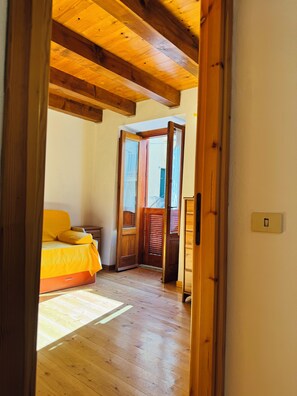 A room with a bed, wooden flooring, a door leading outside, and a light switch on the wall. - Tropea Eye (Tropea)