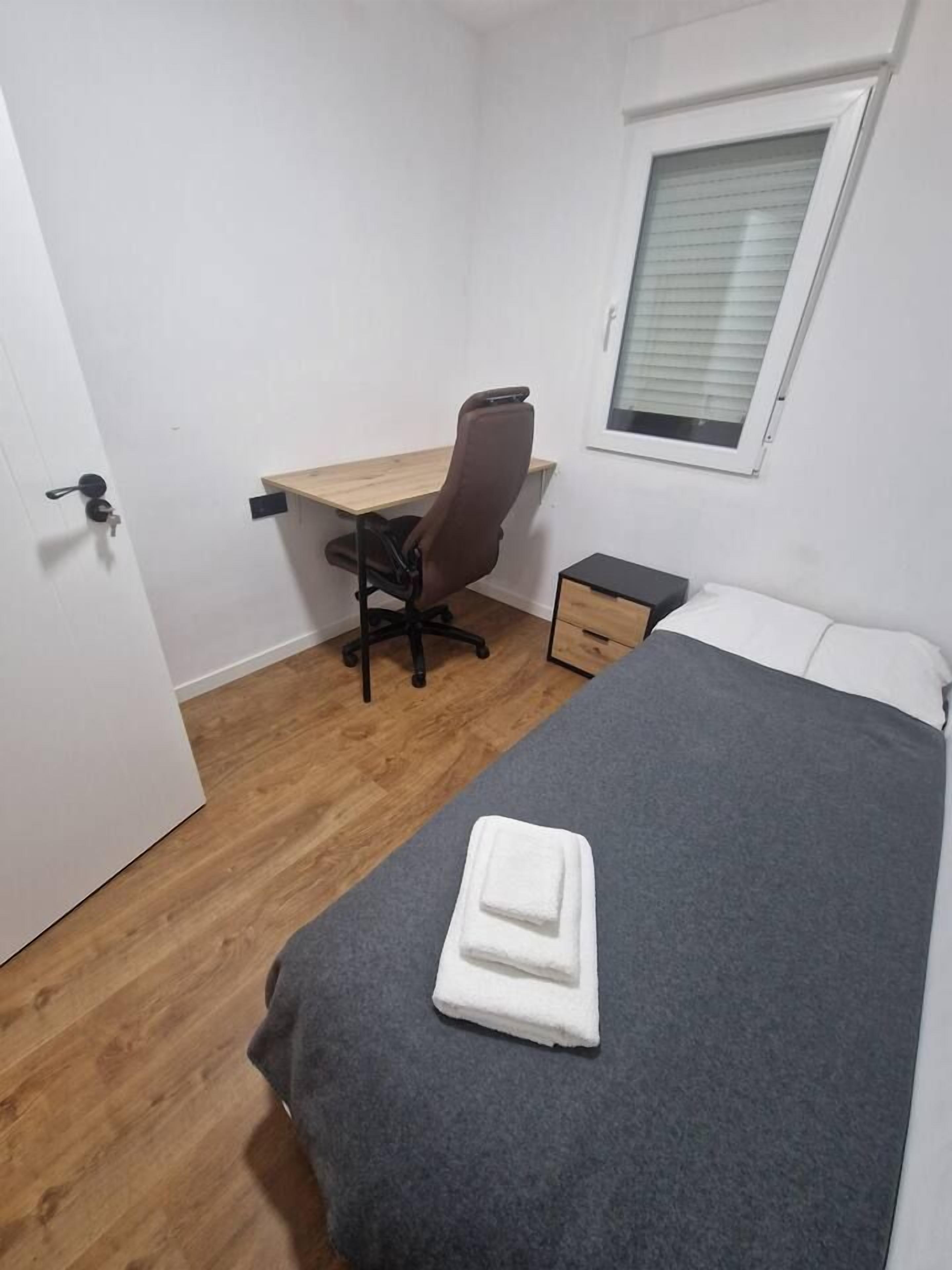 Een slaapkamer met een bed, een bureau en een stoel.