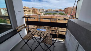 Un balcón con una mesa y sillas de madera, un cartel que indica zona de fumadores y vistas de edificios circundantes.