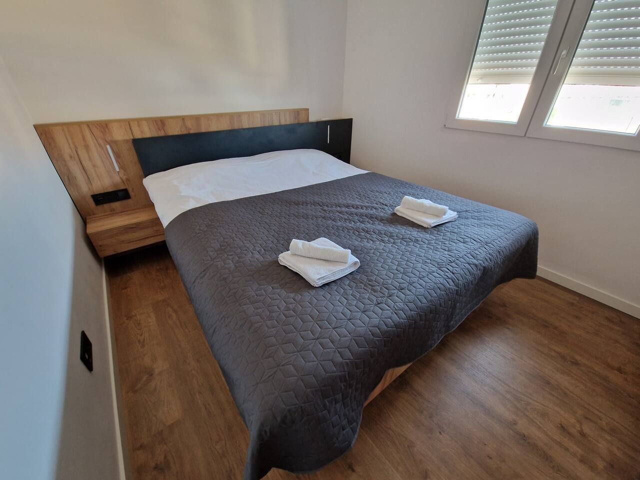 Una cama individual con colcha acolchada oscura y dos toallas blancas dobladas con cuidado.