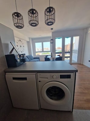 Une cuisine compacte équipée d’un lave-linge, un coin repas avec une table et des chaises, et une grande fenêtre offrant une belle vue.