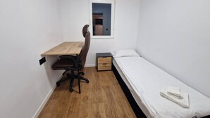 Una habitación pequeña con un escritorio de madera, una silla, una cama individual y un ventanal.