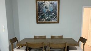 Ein Essbereich mit einem rechteckigen Holztisch und sechs Stühlen, einem gerahmten Bild an der Wand und einem hellen Boden.