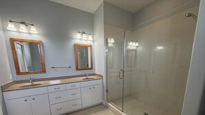 Ein Badezimmer mit einem Doppelwaschbecken, zwei Spiegeln, einer Duschkabine aus Glas und einem Holzboden in Hellton.