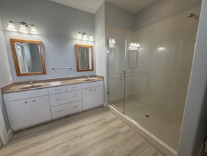 Ein Badezimmer mit einem Doppelwaschbecken, zwei Spiegeln, einer Duschkabine aus Glas und einem Holzboden in Hellton.