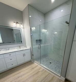 Une salle de bain moderne avec une douche à parois de verre, un meuble-lavabo en marbre et un grand miroir.