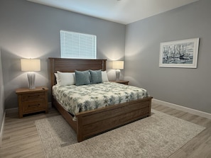A bedroom with a wooden bed, two bedside tables with lamps, a window with blinds, and a framed picture on the wall. - Pool + Dock + 3 Bedrooms + No Bridge Gulf access (Englewood)