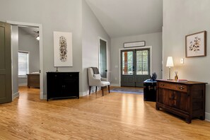 Ein geräumiger Raum mit Holzboden, einem schwarzen Schminktisch, einem weißen Stuhl und einer Tür mit Fenster.