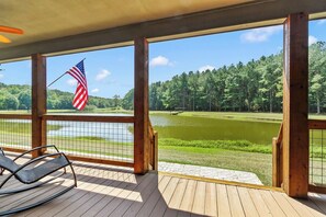 Eine Holzterrasse mit Blick auf einen See und einen Golfplatz, eine amerikanische Flagge und ein Stuhl.
