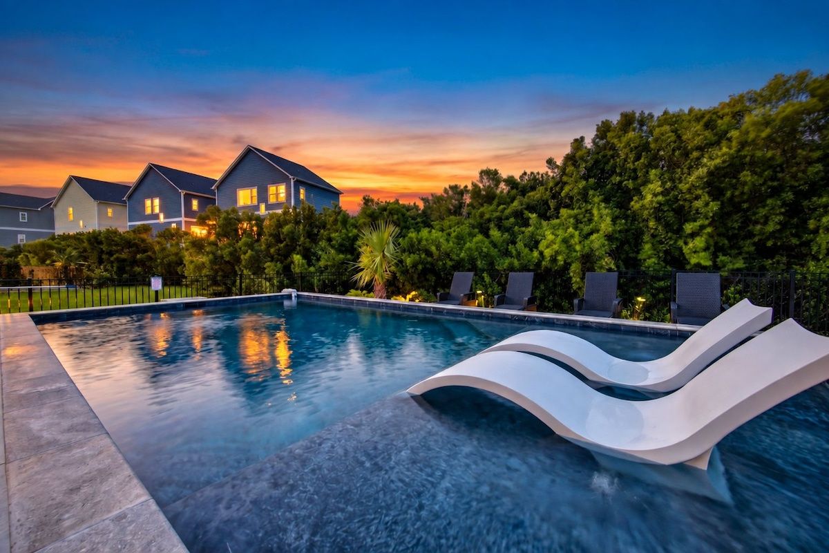 A swimming pool with a modern slide, surrounded by lush greenery and residential buildings.