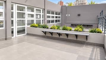 Une terrasse extérieure avec un banc, des plantes en pot et un bâtiment doté de grandes fenêtres.