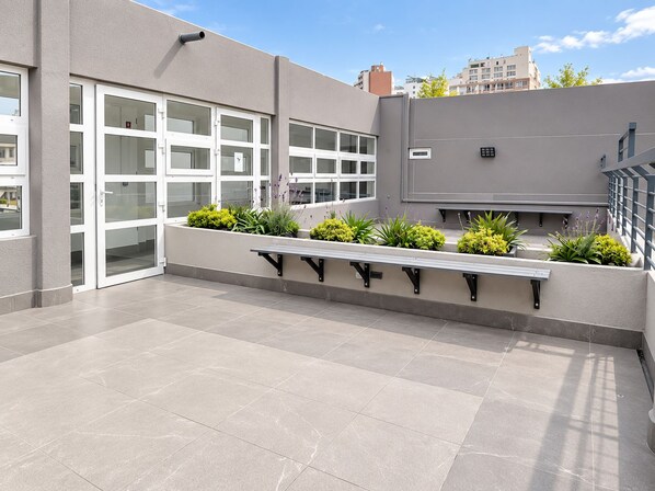 An outdoor terrace with a bench, potted plants, and a building with large windows.