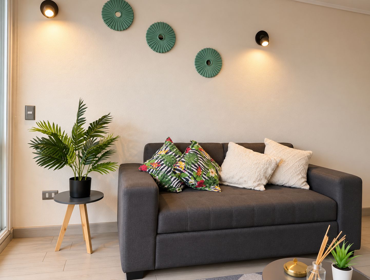 Una sala de estar moderna con un sofá gris, una planta en maceta y luces decorativas en la pared.