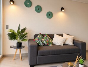 Una sala de estar moderna con un sofá gris, una planta en maceta y luces decorativas en la pared.
