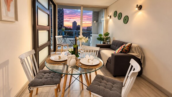 Un comedor con una mesa de vidrio, sillas blancas y un sofá con un cojín colorido.