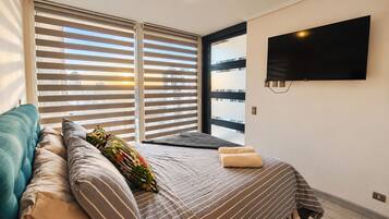 Une chambre d’hôtel avec un lit, un canapé, un téléviseur fixé au mur et une fenêtre avec des stores.