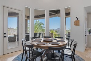 A dining area with a round table, black chairs, and a view of palm trees and mountains through large windows. - Fountain Hills Hideaway: Pool, Views, Game Room (Fountain Hills)