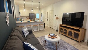 Uma sala de estar moderna com sofá, mesa de centro, televisão e cozinha ao fundo.