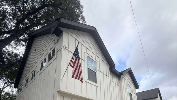 Um edifício de dois andares com fachada branca, telhado preto e uma bandeira americana na lateral.