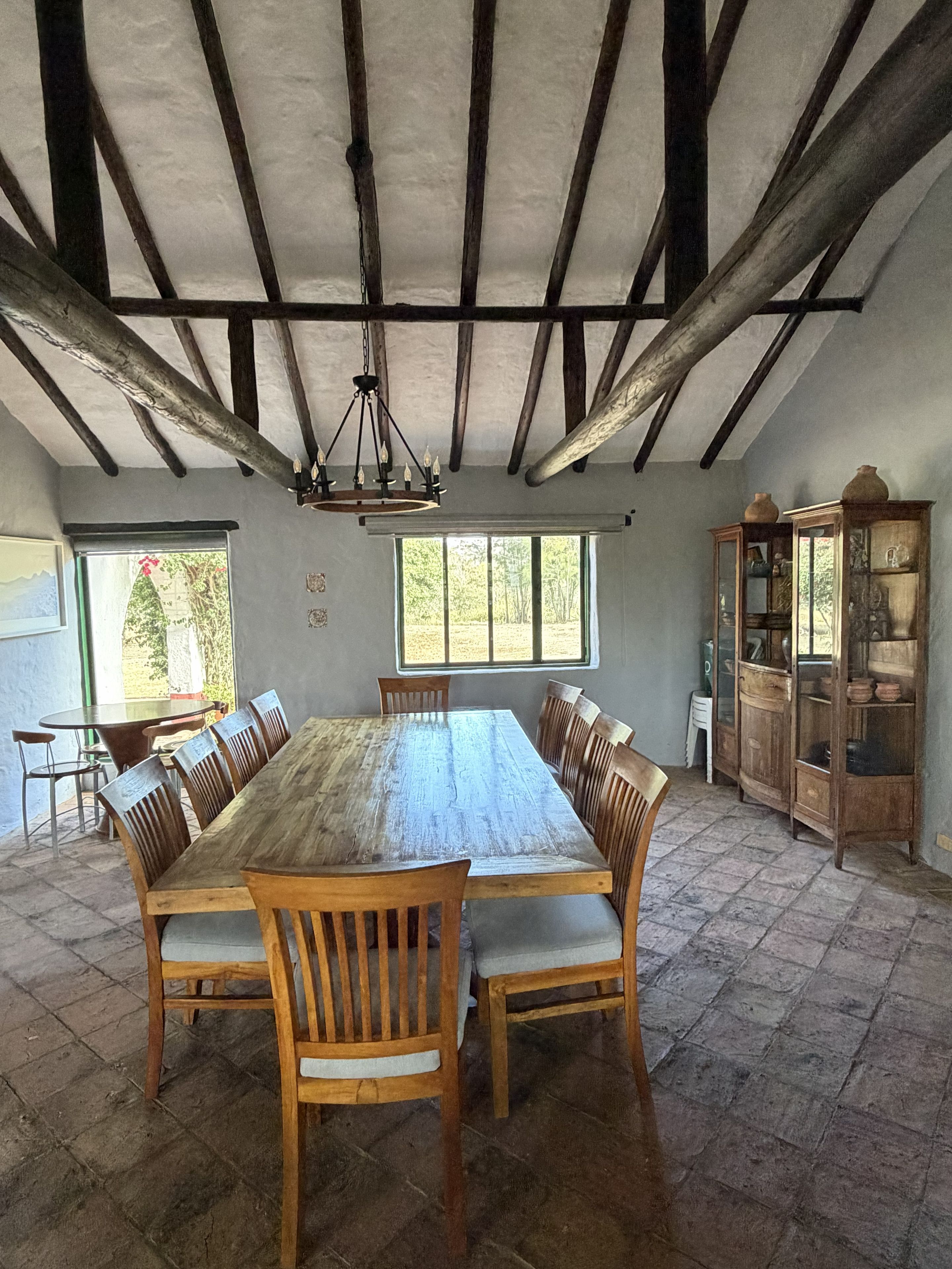 A dining area with a large wooden table and chairs, a chandelier, and a cabinet with glass doors.