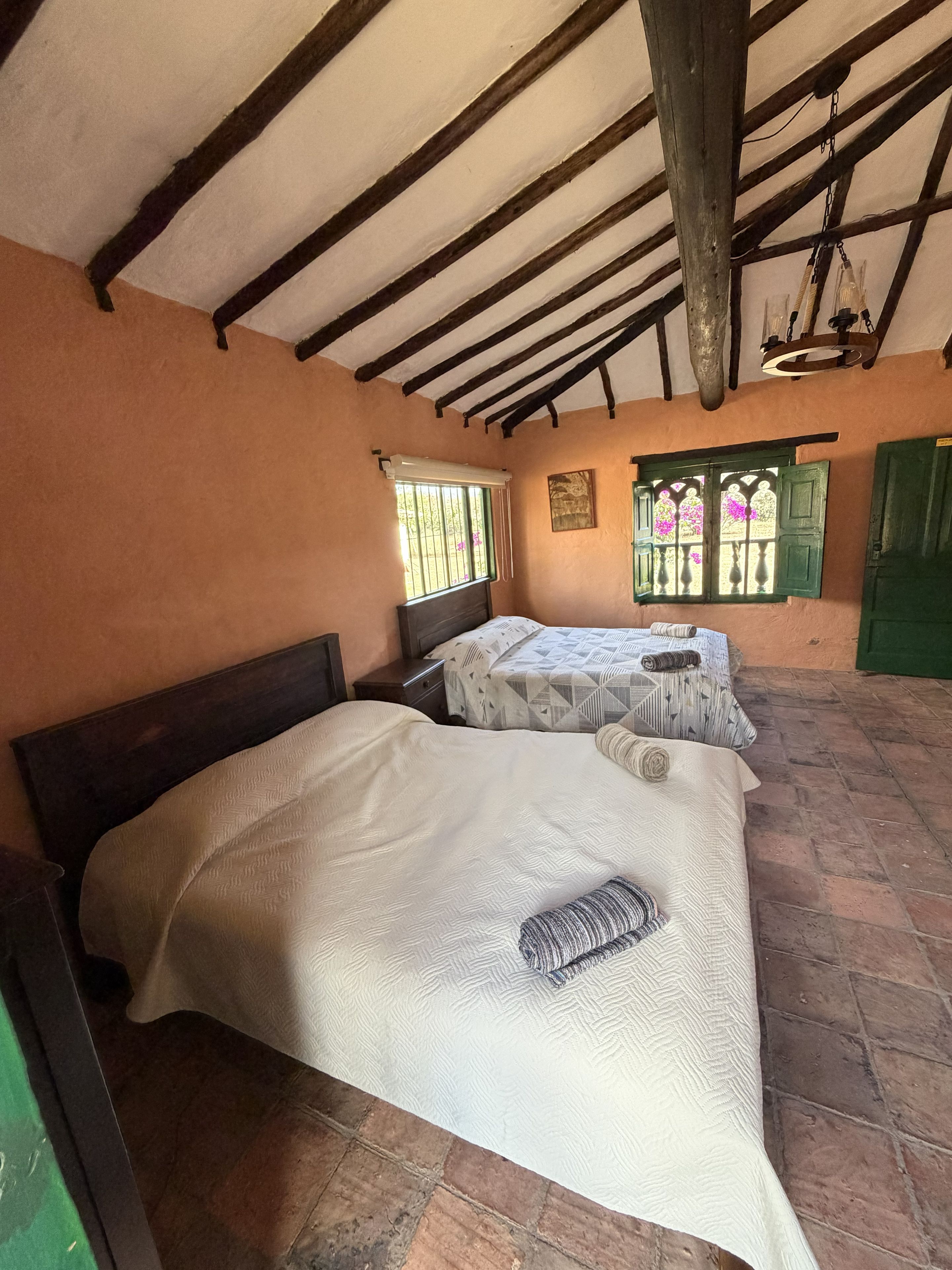 A room with two beds, wooden beams on the ceiling, and a brick floor.