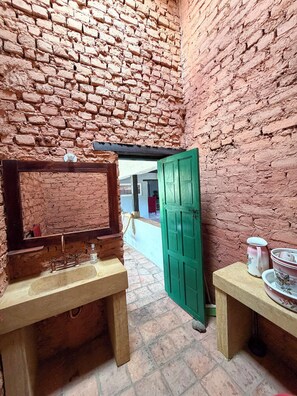 Ein Zimmer mit Backsteinwand, einer Holzbank, einer grünen Tür und einem Waschbecken.