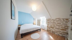 A bedroom with a bed, a round rug, a stone wall, and a window. - Havre de paix - charmante maison avec jardin (Quiberon)