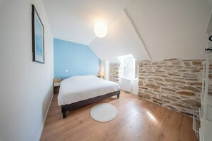 Une chambre avec un lit, un tapis rond, un mur en pierre et une fenêtre.