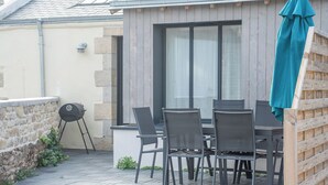An outdoor patio with a table and chairs, a grill, and a wooden fence. - Havre de paix - charmante maison avec jardin (Quiberon)