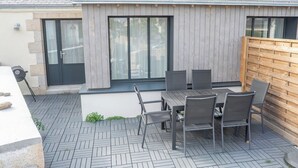 An outdoor patio with a table and chairs, a wooden fence, and a building with a tiled roof. - Havre de paix - charmante maison avec jardin (Quiberon)