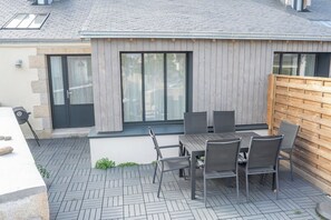 Une terrasse extérieure avec une table et des chaises, une clôture en bois et un bâtiment doté d’un toit en tuiles.