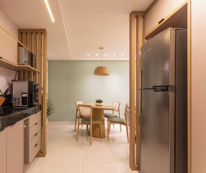 A modern kitchen with a built-in refrigerator, a dining table with chairs, and a hanging pendant light. - Penthouse with jacuzzi, barbecue and sea view. (João Pessoa)