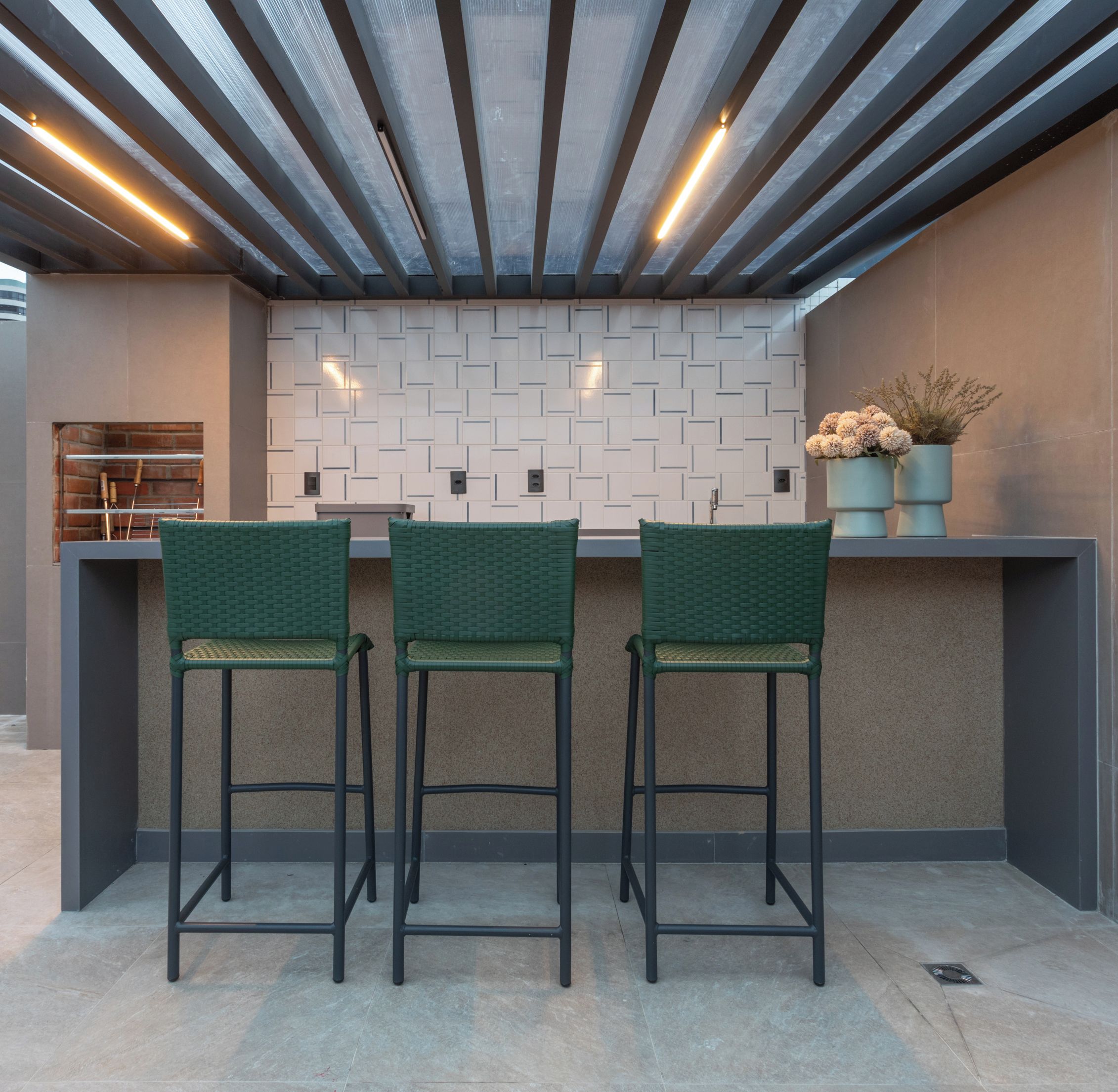 A modern kitchen with a bar area, featuring a patterned backsplash, green bar stools, and overhead lighting.