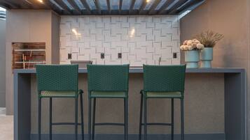 A modern kitchen with a bar area, featuring a patterned backsplash, green bar stools, and overhead lighting.
