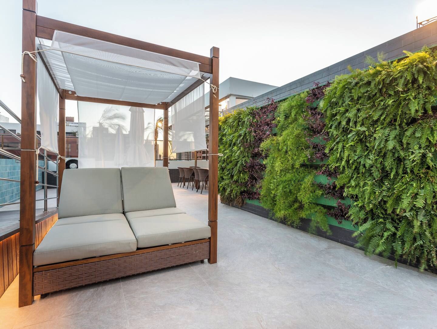 A modern outdoor seating area with a canopy, a green vertical garden, and a view of the cityscape.