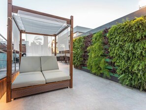 A modern outdoor seating area with a canopy, a green vertical garden, and a view of the cityscape. - Penthouse with jacuzzi, barbecue and sea view. (João Pessoa)