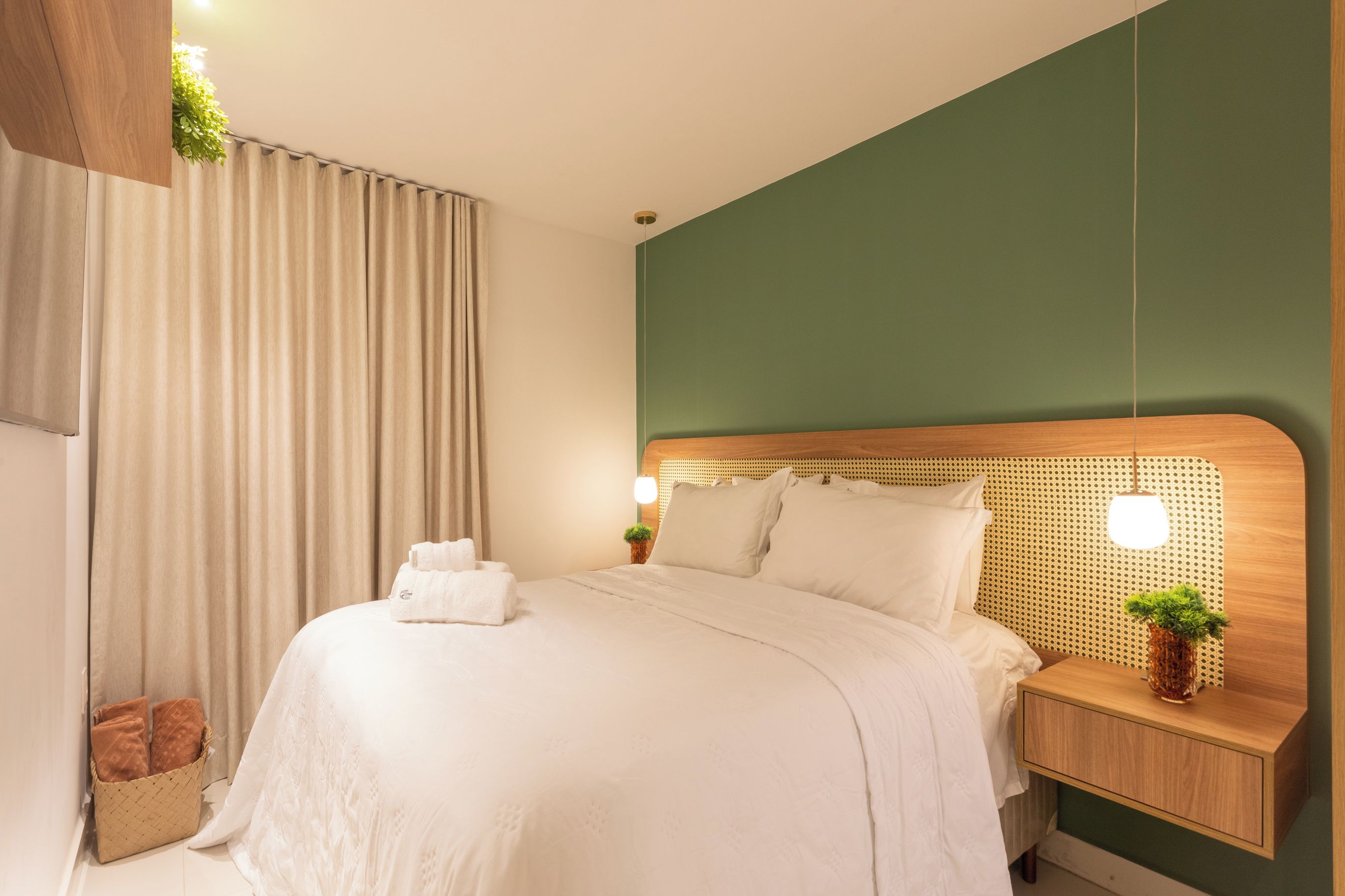 A hotel room with a bed, a nightstand, a lamp, and a potted plant.