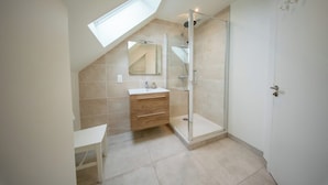A modern bathroom with a skylight, a glass shower enclosure, and a vanity with drawers. - Petit coin de paradis - charmante maison jardin (Quiberon)