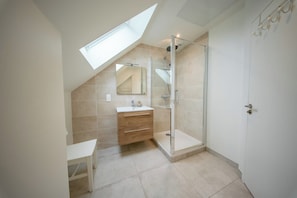 Une salle de bain moderne dotée d’un puits de lumière, d’une douche à parois de verre et d’un meuble-lavabo avec des tiroirs.