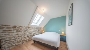 A bedroom with a stone wall, a sloped ceiling, a bed, a nightstand, and a window. - Petit coin de paradis - charmante maison jardin (Quiberon)