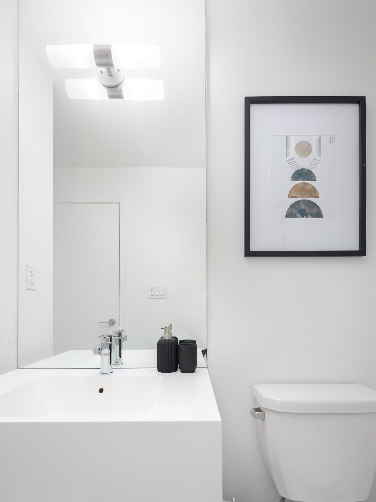 A modern bathroom with a white sink, a toilet, and a framed abstract artwork on the wall.