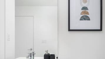 A modern bathroom with a white sink, a toilet, and a framed abstract artwork on the wall.
